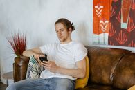 Man in White Crew Neck T-shirt and Blue Denim Jeans Sitting on Brown Sofa