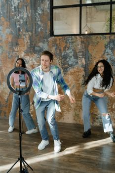 Three young adults dancing indoors, creating social media content using a smartphone and ring light.