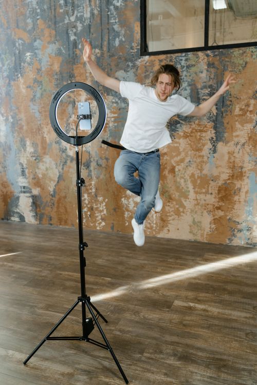 Free Energetic young man jumps beside a ring light setup in a modern studio. Stock Photo