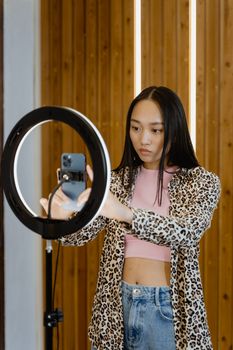 Asian woman using a smartphone and ring light for video creation indoors.