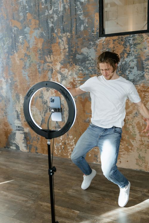Free A young man dancing energetically while filming content indoors using a ring light. Stock Photo