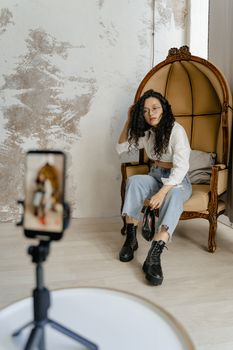 Young woman in trendy outfit sitting on a chair, recording indoors.