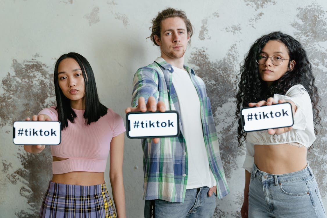 An image of three people facing the camera with #TikTok written on their phone screens. 
