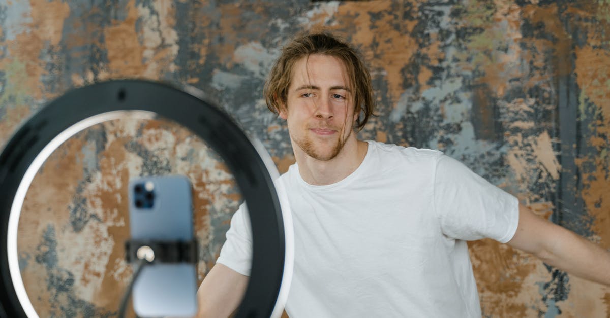 Man filming vlog with smartphone and ring light in an indoor setting. Casual attire.