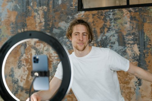 Free Man filming vlog with smartphone and ring light in an indoor setting. Casual attire. Stock Photo