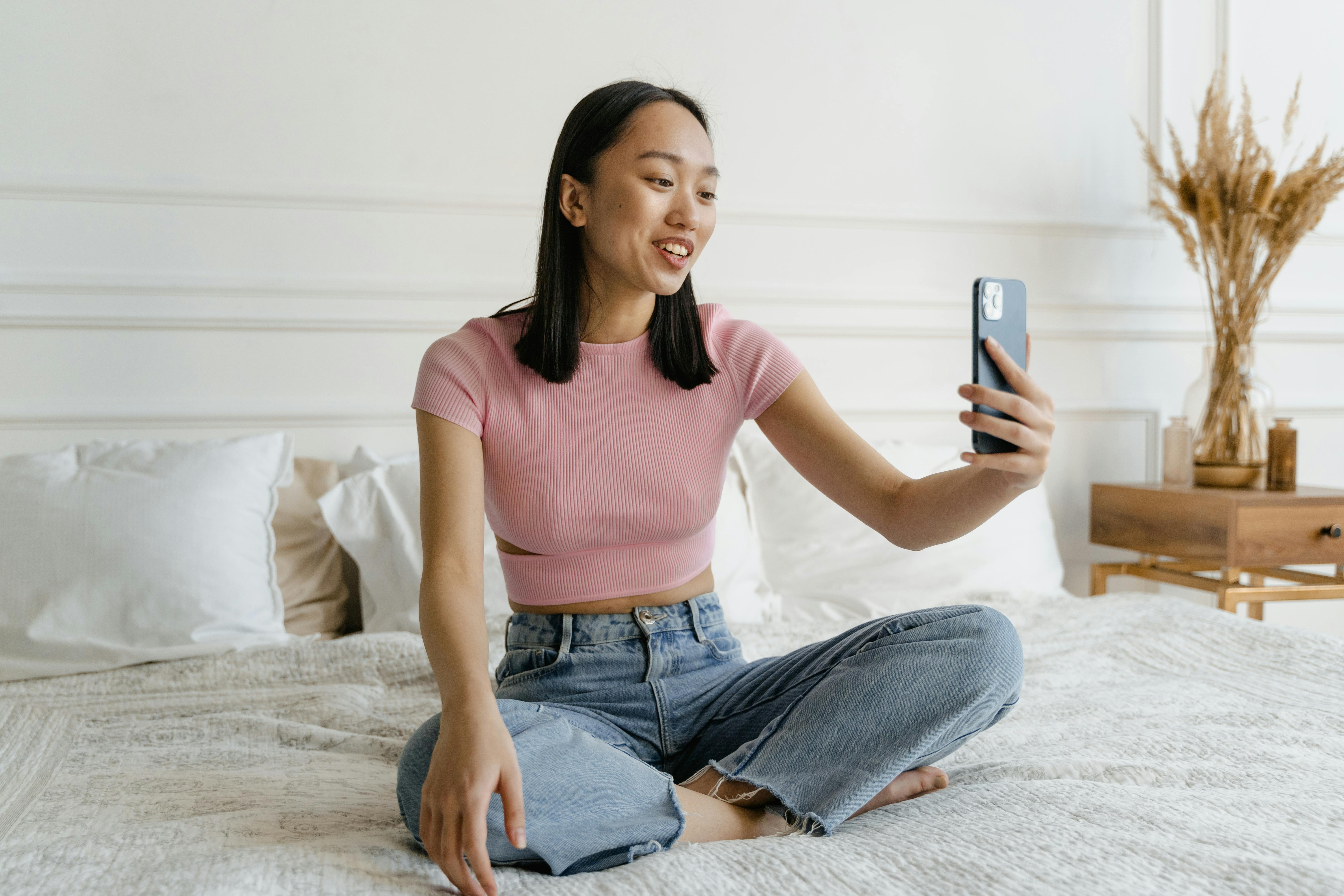 woman in pink crew neck t shirt and blue denim jeans sitting on white bed