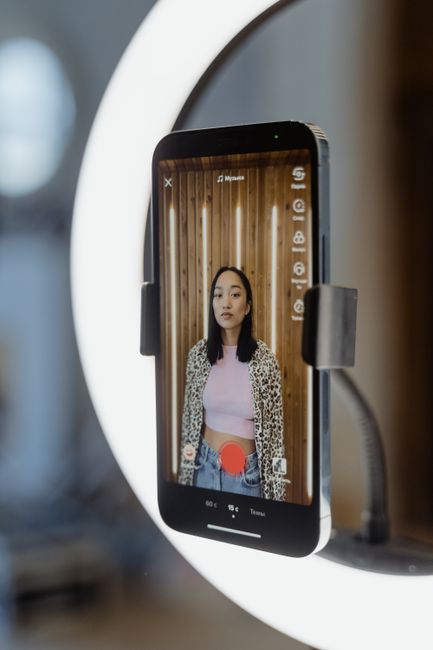 Teenage girl livestreaming content indoors using a smartphone and ring light.