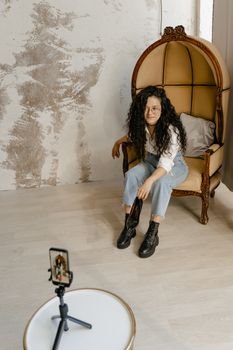 A woman with curly hair uses her smartphone for social media video recording indoors.