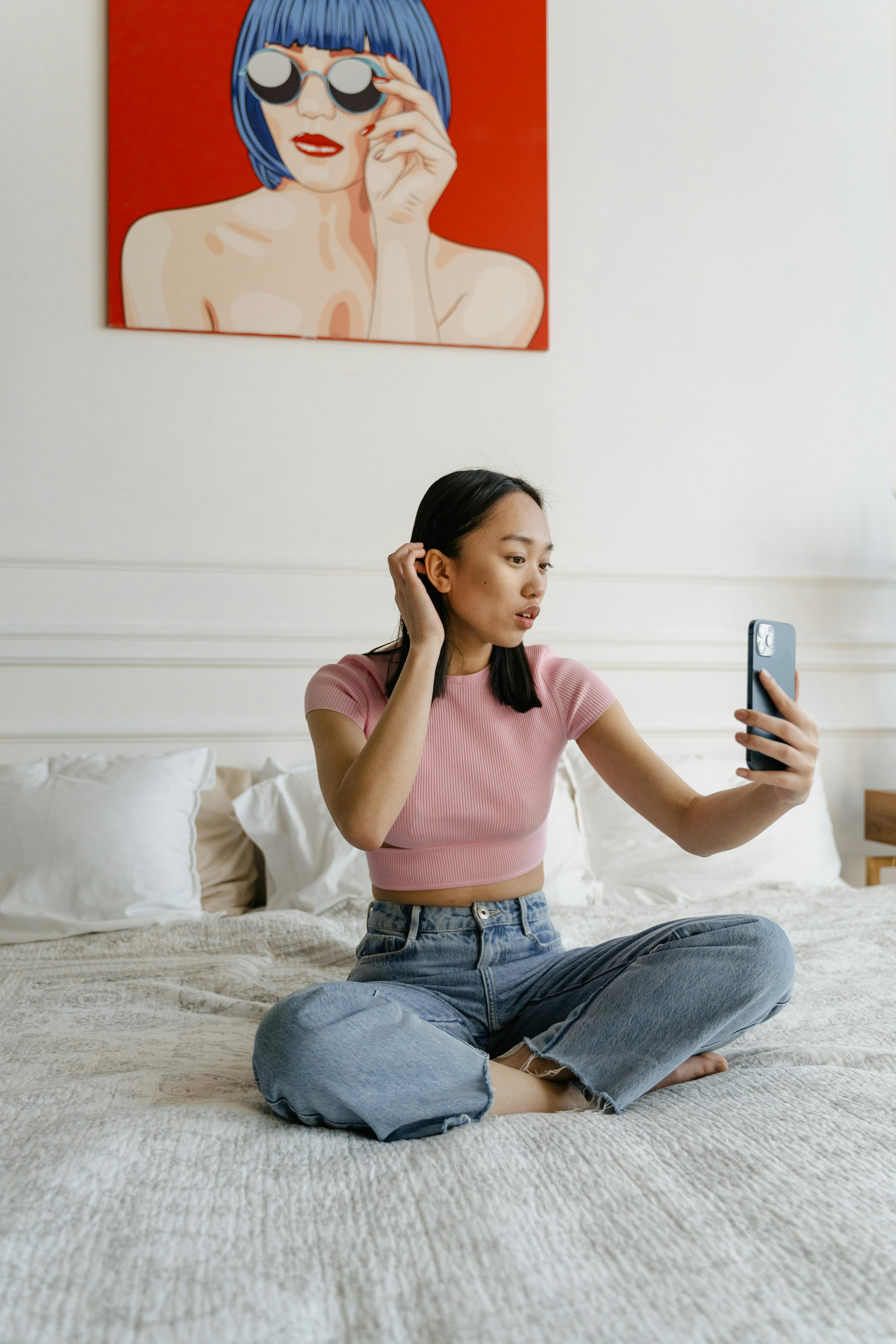 woman in pink long sleeve shirt and blue denim jeans sitting on bed