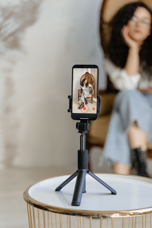 Free Young Asian woman filming content with smartphone on tripod indoors. Stock Photo