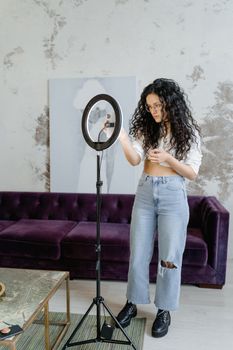 A young woman adjusts a ring light indoors, preparing for a social media video shoot.