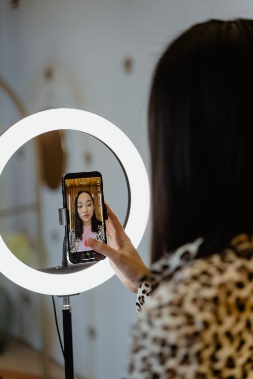Free Young woman recording video with smartphone and ring light indoors. Stock Photo