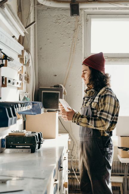 A craftsman stands in a workshop, reading a document with focus. Brightly lit space highlights tools. A craftsman stands in a workshop, reading a document with focus. Brightly lit space highlights tools.