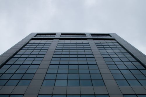 Free Low-angle view of a modern skyscraper with a sleek glass facade set against a cloudy sky. Stock Photo