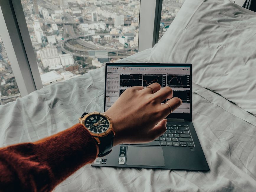 How Personal Capital Solves Net Worth Tracking Challenges for Investors A person checks time while trading on a laptop with charts, overlooking a city view from bed.