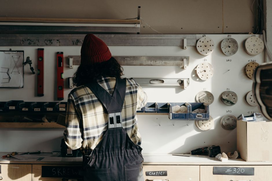 A craftsman in a beanie works in a tool-filled workshop, focused on a carpentry project.