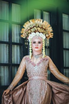 Portrait of a bride in traditional Indonesian dress with ornate headdress, elegantly poised indoors.