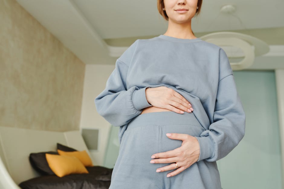 adult respite care - A close-up of a pregnant woman indoors, wearing a blue sweater, hand resting on her belly.