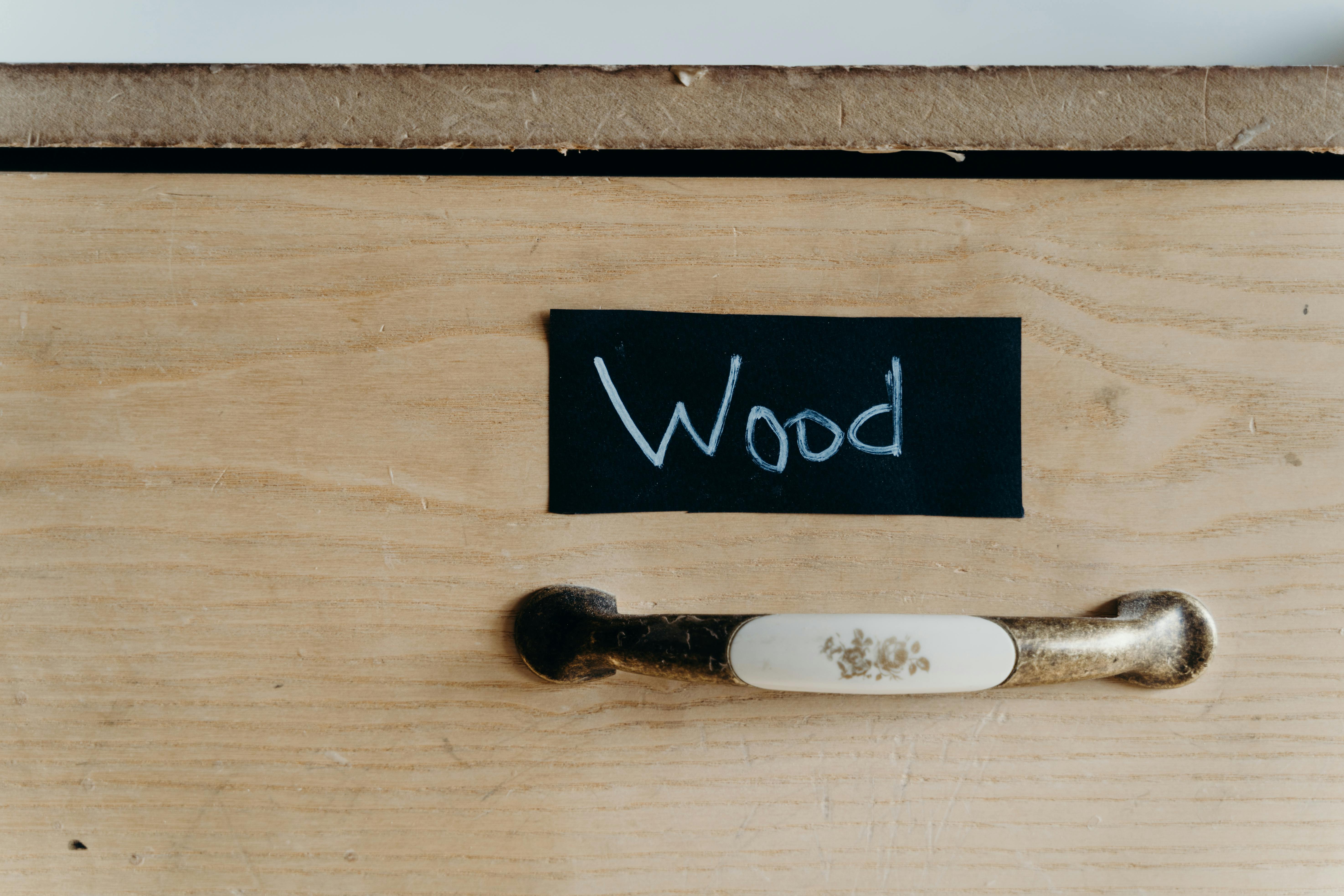 Detailed view of a wooden cabinet drawer with chalk-labeled sign and vintage handle.