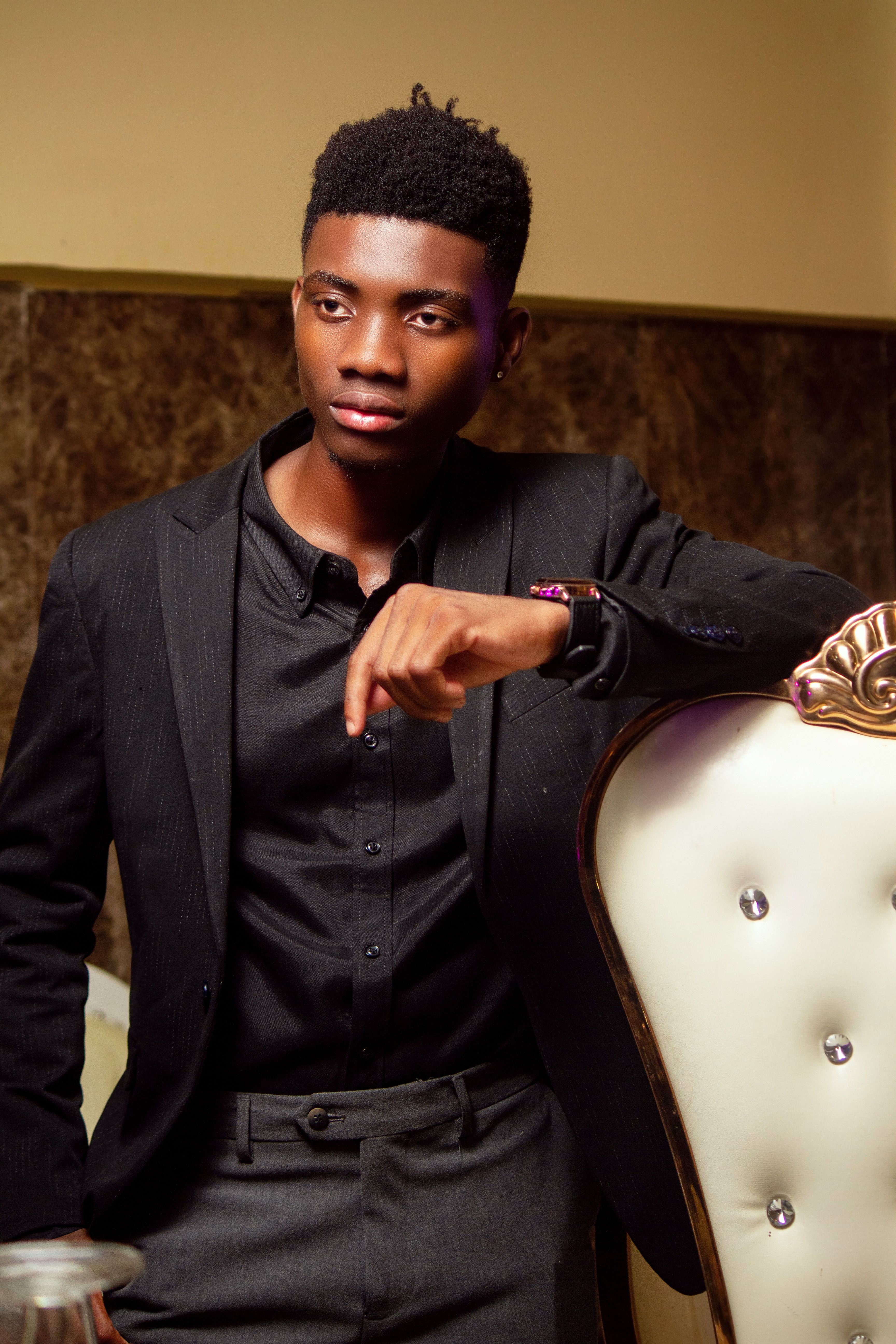 Portrait of a fashionable young man in a black suit, posing confidently indoors.