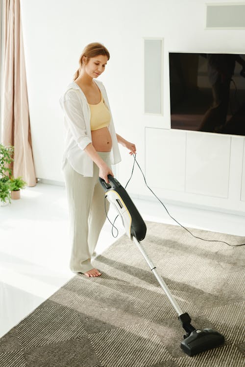 Woman in White Tank Top and White Pants Holding Vacuum Cleaner