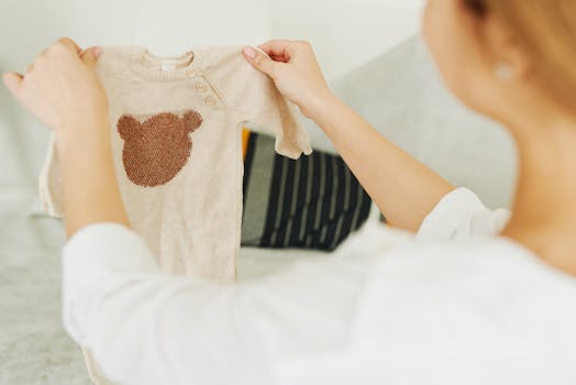 Woman examining a beige baby jumper with a teddy bear design, showcasing cute baby clothing.