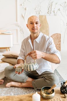Man in a light setting enjoying a tea ceremony at home, embodying relaxation and mindfulness.