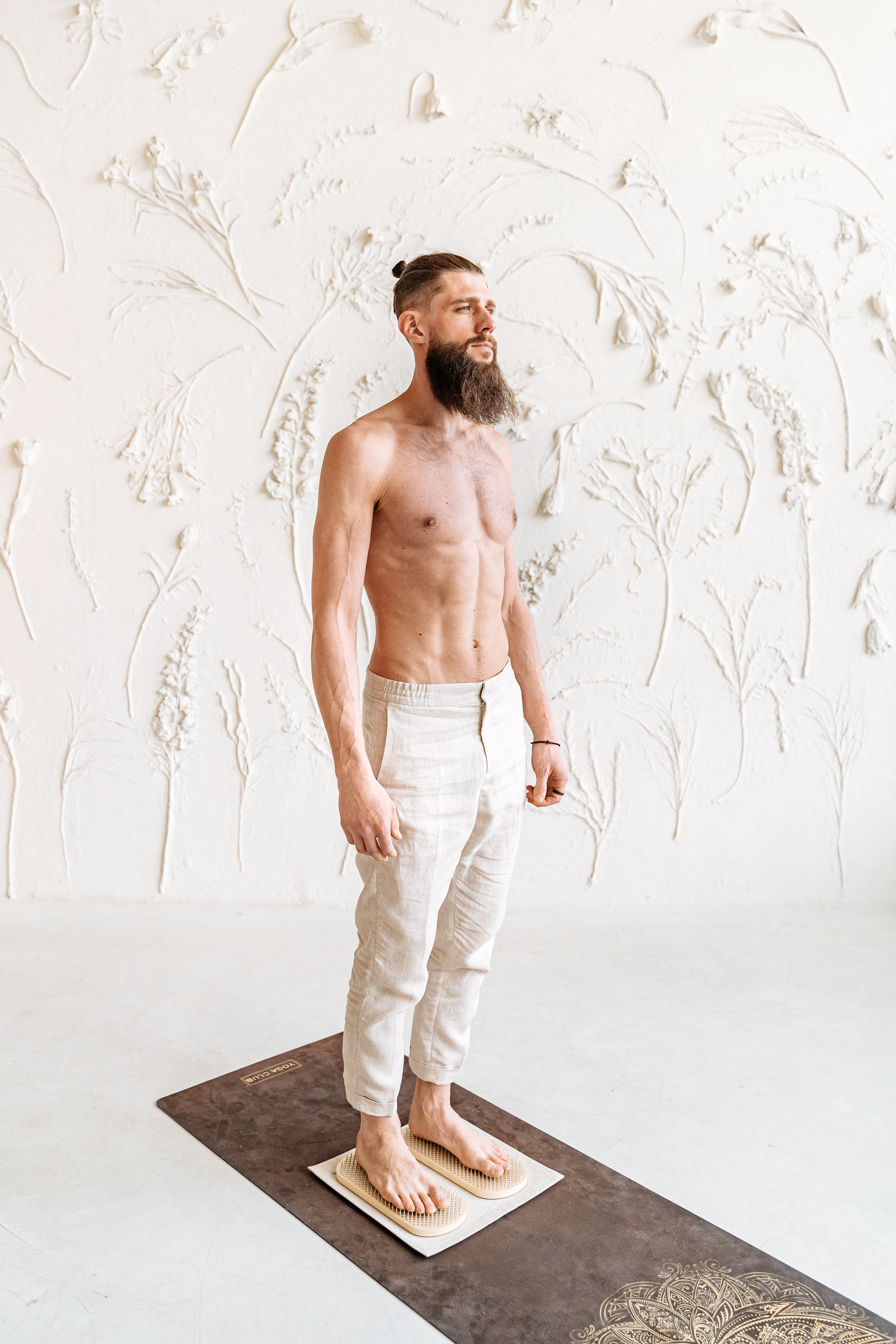 Shirtless bearded man standing on a board for therapy and balance indoors.