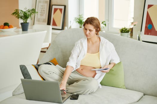 Pregnant woman sitting on sofa working on laptop in cozy home setting.