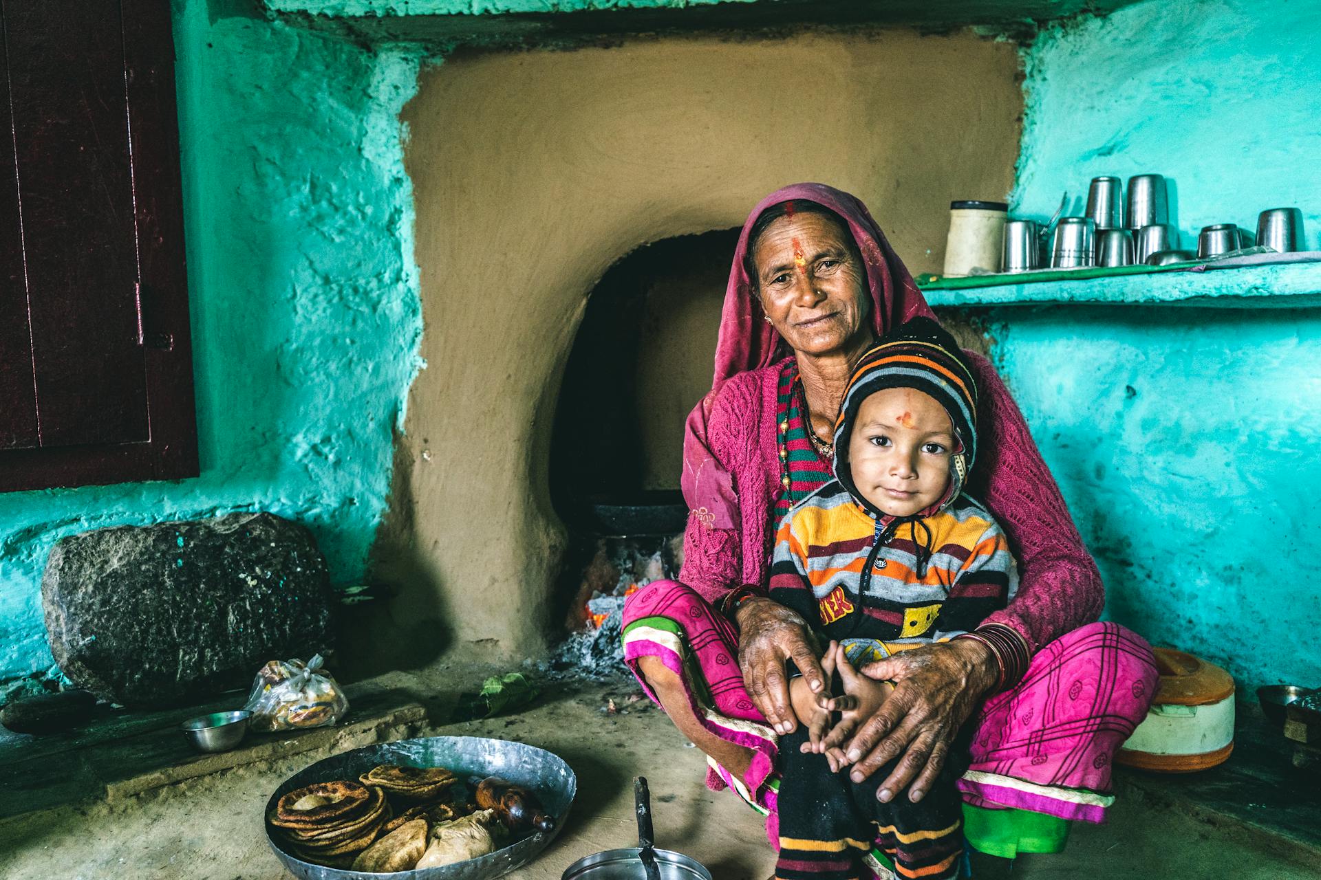 A grandmother and child sit together in a traditional Indian kitchen, showcasing rural lifestyle.