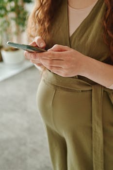 Close-up of a pregnant woman holding a smartphone inside a cozy room.