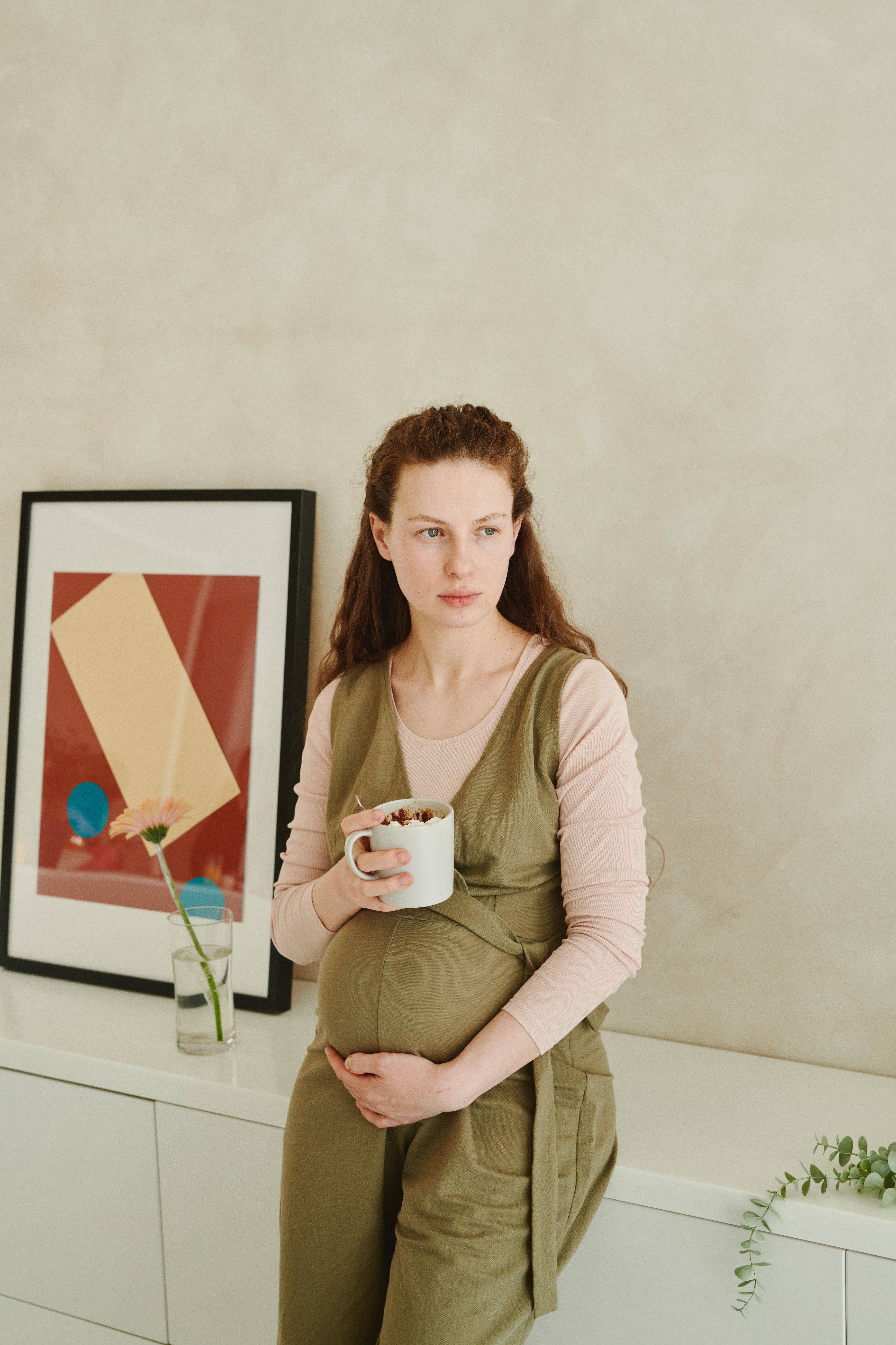 A pregnant woman holding a cup while standing indoors, embodying peaceful maternity.