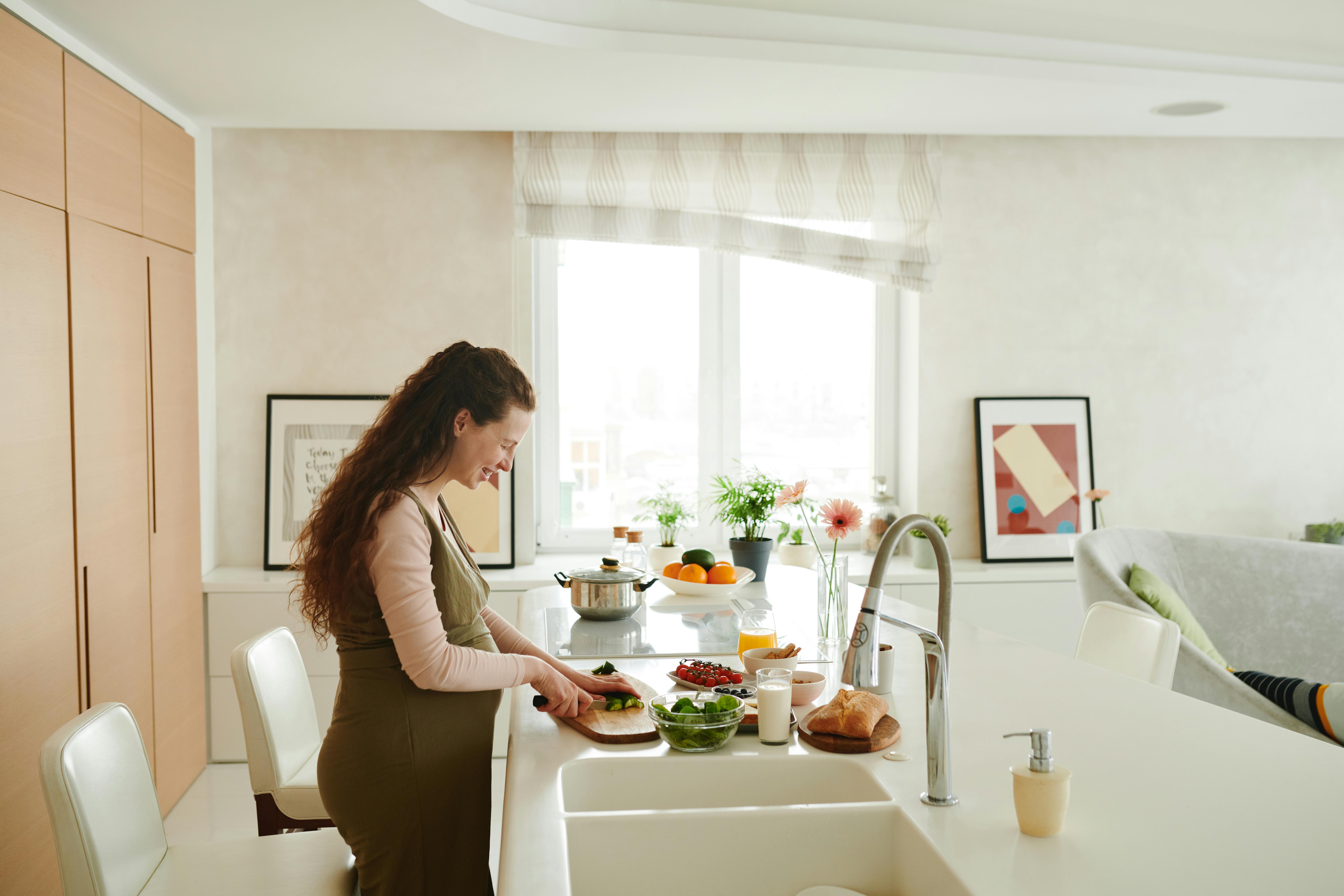 Pregnant woman slicing vegetables in a bright kitchen setting, embracing healthy lifestyle.