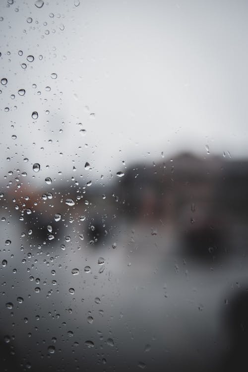 Blurred wet window with raindrops and vague gray view through glass in rainy weather
