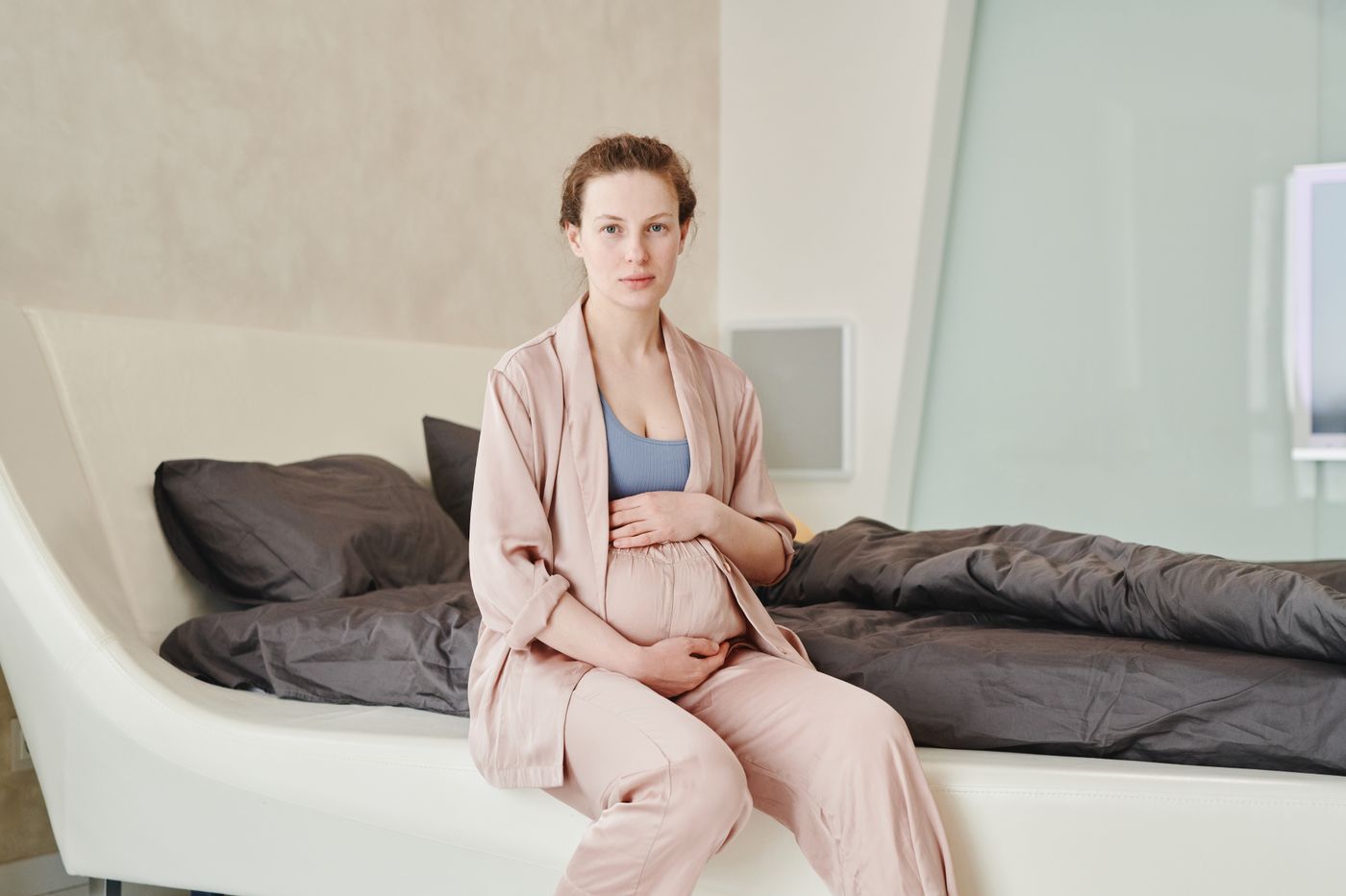 Future maman installée sur son lit dans une chambre lumineuse et naturelle