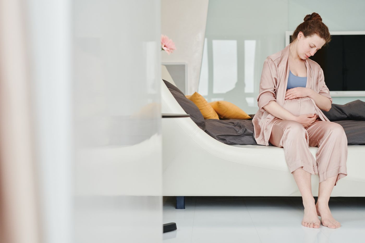 Future maman assise sur son lit en soutenant doucement son ventre