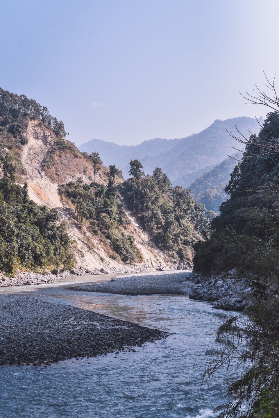 A river braiding around a broad pale shingle spit between steep forested hills in Sikkim