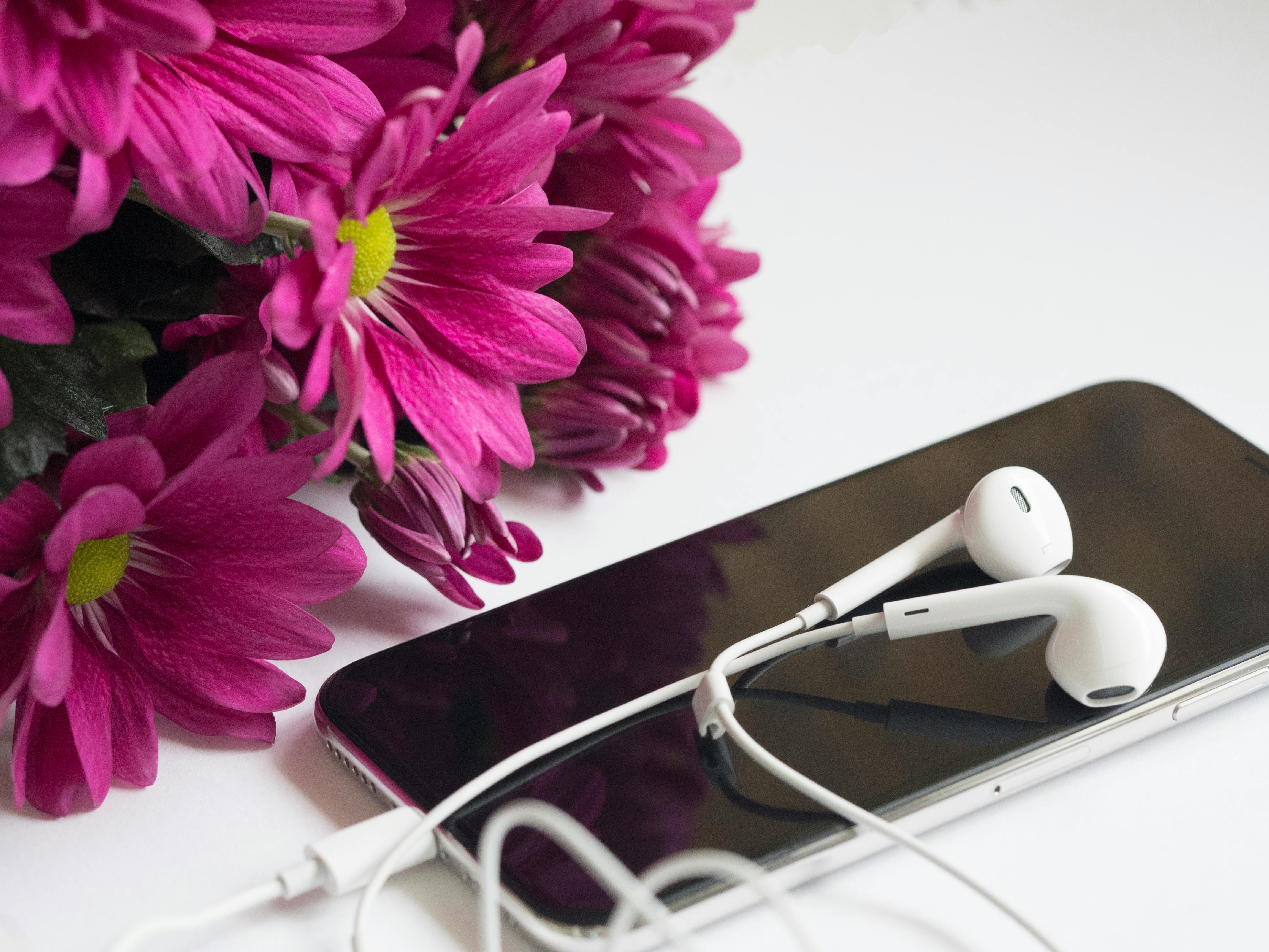 Close Up Photography Of Earphones On Top Of Iphone 6 Near Flowers