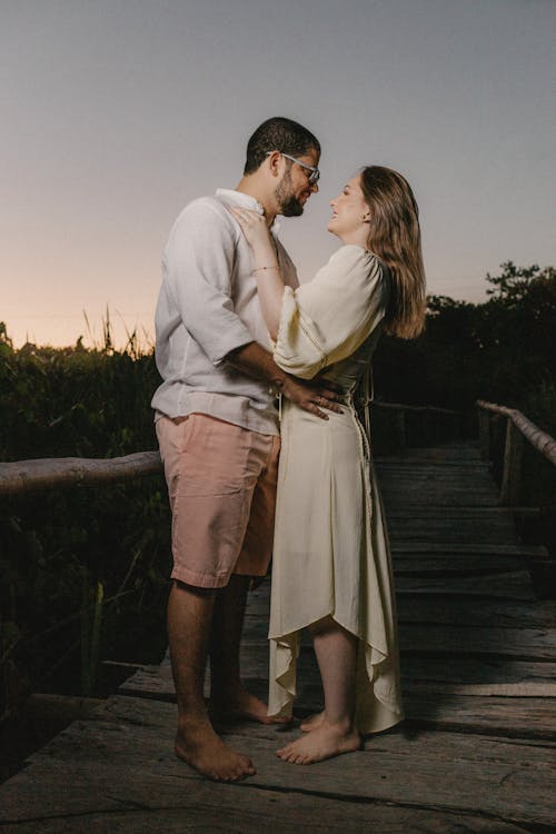 Full body side view of happy couple hugging while standing on wooden walkway and looking at each other