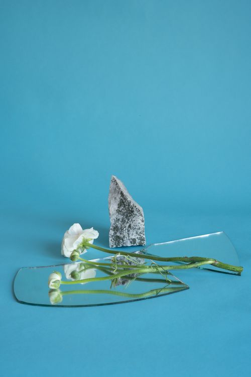 Free A minimalist composition with white flowers, a stone, and mirror on blue background. Stock Photo