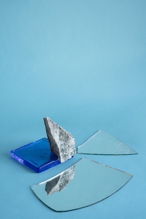A Broken Mirror and Stone on Light Blue Background
