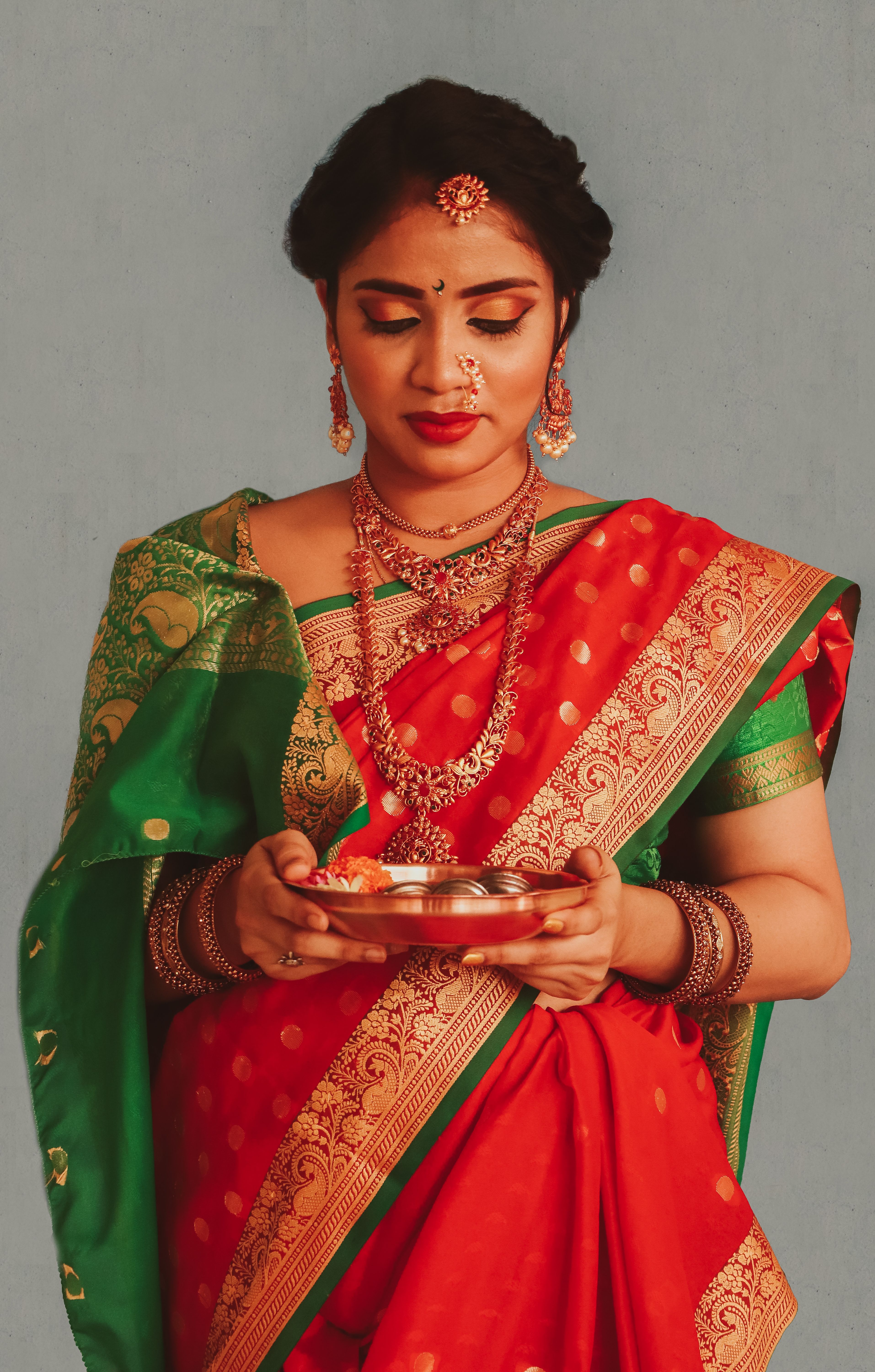 Portrait of a culturally dressed Indian woman in a red and green saree, holding traditional diyas.