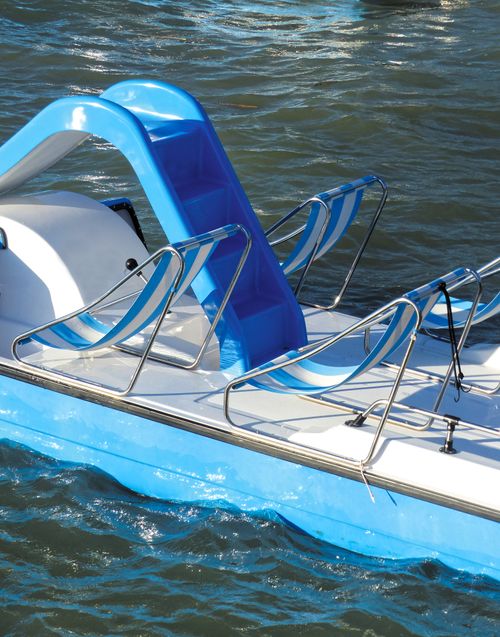 Free A vibrant blue paddle boat with a slide, situated on calm lake waters in bright sunlight. Stock Photo