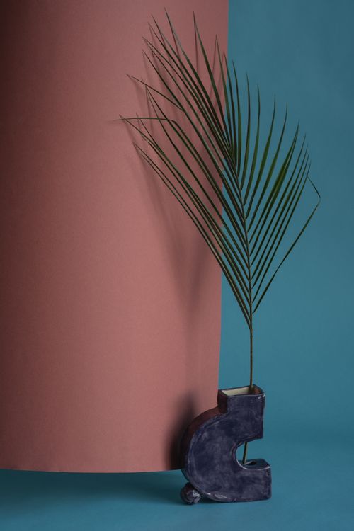Free A single palm leaf in a unique abstract vase against a color-blocked background. Stock Photo