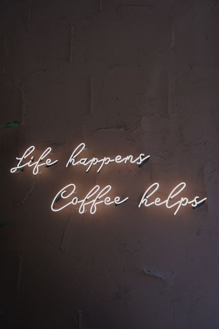 Illuminated neon sign reading 'Life happens, coffee helps' on dark wall background.