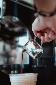 Close-up of a barista pouring espresso into a latte in a café setting.