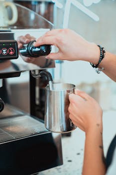 Close-up of a barista steaming milk in a jug at a coffee shop, showcasing barista skills and coffee preparation.