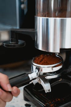 Close-up of coffee grinder dispensing grounds into portafilter, illustrating coffee preparation.
