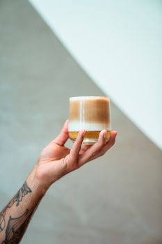 A tattooed hand holding a refreshing iced latte against a neutral background.