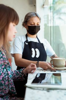 Barista wearing a face mask serving coffee to a customer in a contemporary café setting.